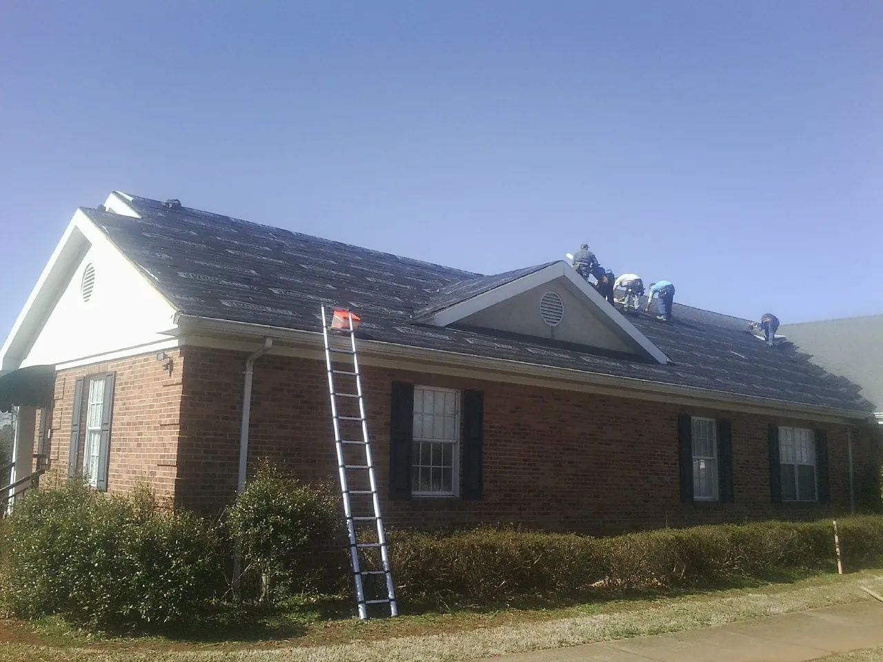 Crew tearing shingles off a brick ranch roof with a ladder set — Metal Roof Repair work by our crew in Joliet