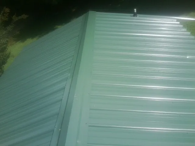 New green metal panels meeting at the ridge of a roof — Flat Roof Repair work by our crew in Joliet