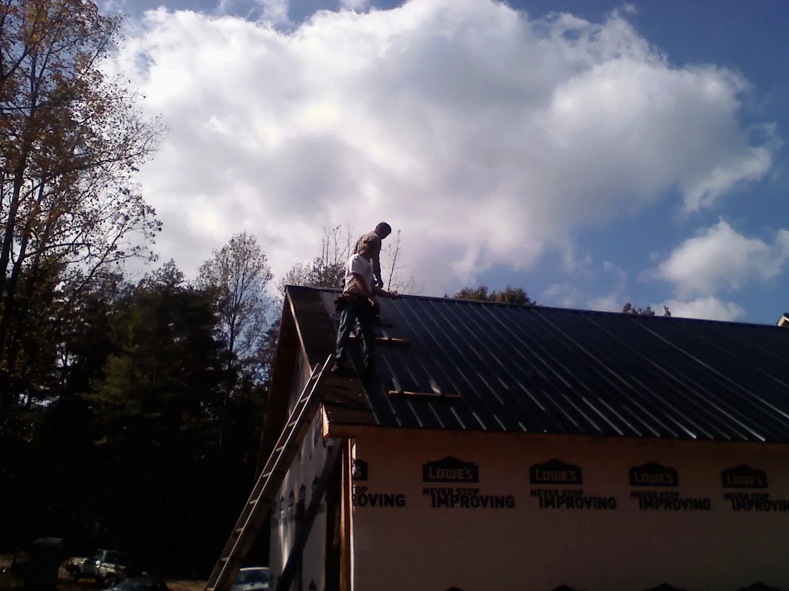 Roofer fastening dark metal panels high against a cloudy sky, from a Roof Inspection job in Joliet