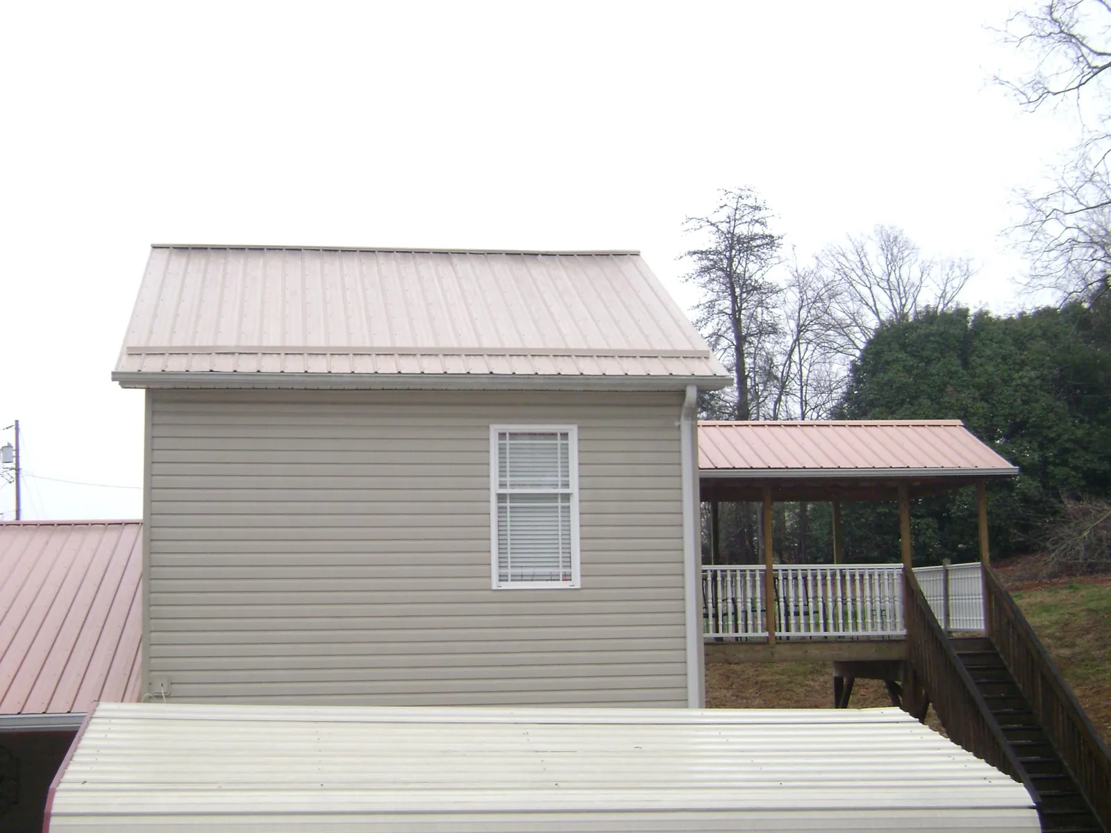 Tan metal roofs on a two story addition and attached porch, from a Roof Replacement job in Joliet